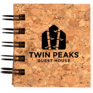 A cork notebook featuring a black spiral binding and the logo for "Twin Peaks Guest House" embossed on the cover.