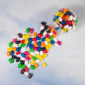 A container spilling assorted colour mini jelly beans in vibrant hues of pink, yellow, green, blue, and more.