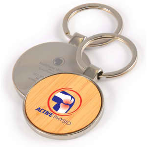 A circular bamboo keytag with a silver metal ring, featuring a logo on a wooden surface.