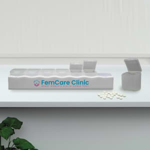 A white weekly pill box with multiple compartments, featuring a logo and a few pills scattered nearby.