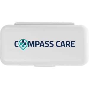 A compact pill organizer featuring a white exterior with a logo that reads "COMPASS CARE."