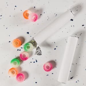 Colorful gummi fruit rings in assorted flavors scattered on a speckled surface, with packaging partially visible.