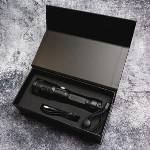 A black rechargeable torch with a charging cable, sitting inside a black box with cushioning.