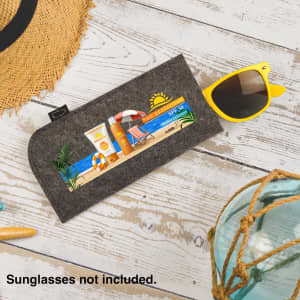 A grey felt sunglass pouch with a seaside graphic design and a logo. Sunglasses not included.