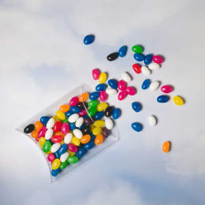Assorted Colour Mini Jelly Beans in a clear pillow pack, with colorful jelly beans scattered around.