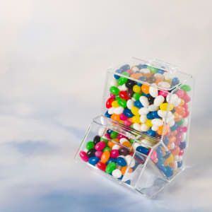 A clear dispenser filled with assorted color mini jelly beans in various shades, including red, blue, green, and white.