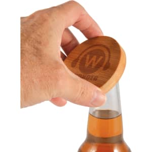 A drink bottle opener coaster in bamboo with a hand positioned above it, showing its natural wood color and branding.