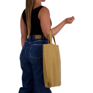 A woman holds a mustard yellow eco-friendly shopping bag with short handles, wearing a black top and blue jeans.