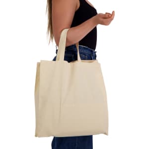 A calico bag with short handles, in a natural beige colour, held by a person. The bag is simple and unbranded.