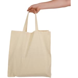 A hand holds a cream-coloured calico bag with short handles, featuring a simple design and no visible branding.