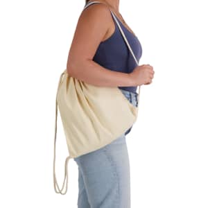 A person is holding a cream drawstring backpack, designed for casual use, featuring a simple style and shoulder straps.