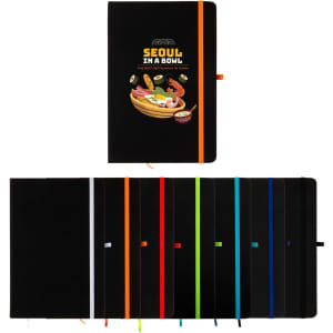 A black A5 notebook with an orange elastic band, featuring colourful variants stacked behind it.