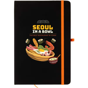 A black A5 notebook with an illustrated cover featuring food items and a logo. It has an orange elastic band.
