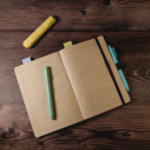 An A5 notebook with yellow and green highlighters, blue and yellow tabs, placed on a wooden surface.