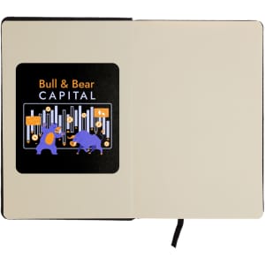 An A5 notebook with a black cover and an illustration featuring a bull and bear on the inner page, includes a logo.
