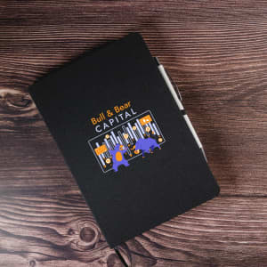 A black A5 notebook with an illustration on the cover and a white pen beside it.
