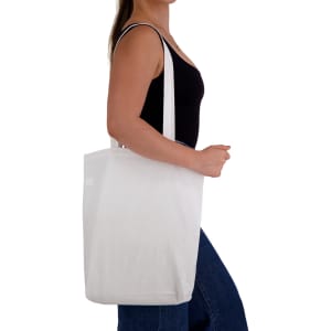 A white cotton long handle bag, held by a person wearing a black top, with the bag's branding visible.