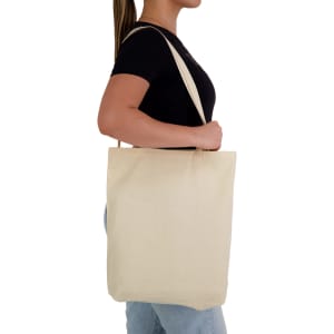 A cream-coloured tote bag with long handles, held by a person against a plain background.