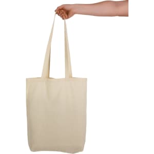 A cream-coloured tote bag with long handles held by a hand. The bag includes a logo.