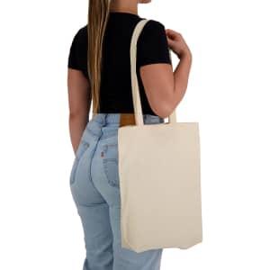 A woman holds a natural-coloured calico tote bag over her shoulder, featuring long handles and a simple design.