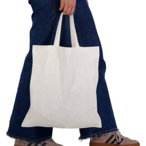 A white short handle bamboo tote bag held by a person wearing denim jeans and sneakers.