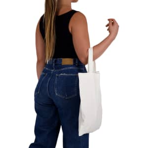 A woman with long hair holds a plain white short handle bamboo tote bag while wearing a black top and blue jeans.