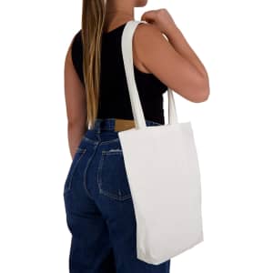 A white tote bag with long handles is being held by a person wearing a black top and blue jeans.
