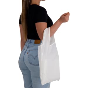 A woman holding a white reusable grocery bag while wearing a black top and light blue jeans. The bag has a logo.