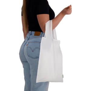 A white reusable grocery bag is held by a person wearing a black top and light blue jeans, with a visible logo.