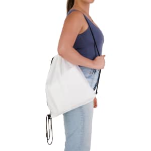 A white drawstring backpack is held by a person wearing a blue top and jeans, featuring a simple design with a logo.