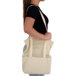 A cream tote bag with mesh panels is being held by a person. The bag has shoulder straps and a spacious design.
