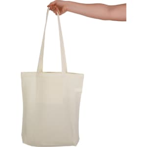 A cream-coloured tote bag with long handles and a pocket, held by a hand. It features a logo.