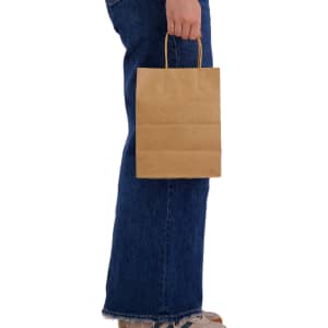 A medium brown paper bag with handles is held by a person wearing jeans. The bag has a plain design.