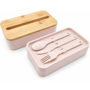 A pink lunch box with a bamboo lid includes a compartment for utensils: a spoon, fork, and knife.