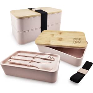 A pink eco lunch box featuring a bamboo lid, with separate compartments and included utensils. It has a black strap for closure.
