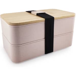 A stacked pink lunch box with a bamboo lid, secured with a black strap, featuring a minimalist design.