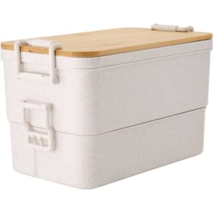A dual-compartment lunch box in white with a bamboo lid, featuring a secure latch and branding.