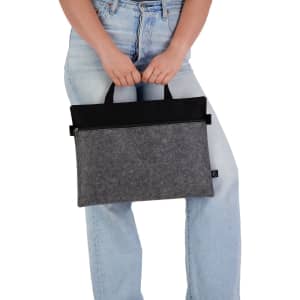 A grey and black felt satchel is held by a person wearing light blue jeans, featuring top handles for easy carrying.