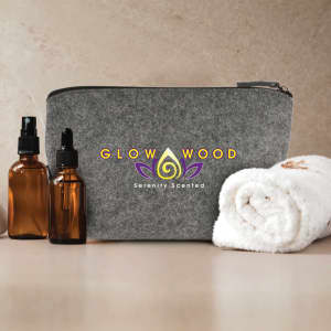A grey felt cosmetic bag with a logo, accompanied by brown glass bottles and a white towel.
