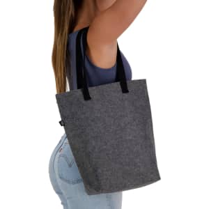 A grey tote bag with black handles, held by a person, featuring a logo on the side.