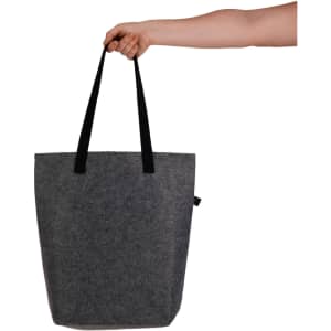 A hand holds a grey felt tote bag with black straps. The bag features a branding logo.