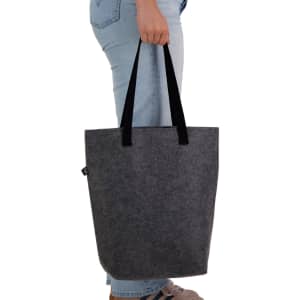 A grey tote bag with black handles, being held by a person wearing blue jeans. The bag has a logo.