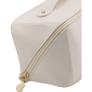 A cream toiletry bag featuring a gold zipper and a branded tag. The bag has a geometric shape and smooth finish.