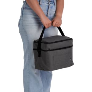 A grey cooler bag with a handle is being held by a person wearing light blue jeans. The bag features a front pocket and branding.