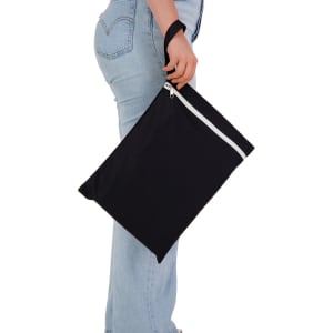 A black Cosi Wet Bag is held by a person wearing light-wash jeans, featuring a white zip and a sturdy handle.