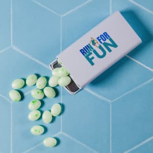 A flip top tin containing green spearmint mints, with some mints spilled onto a light blue surface.
