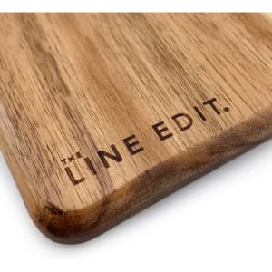 A wooden serving board with a smooth acacia finish featuring a branding logo.