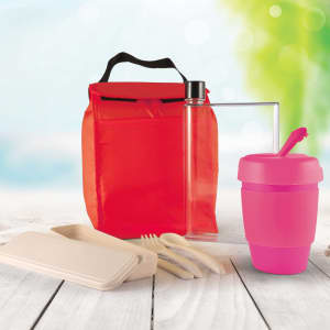 A red picnic bag contains a clear drink bottle, a pink cup with a straw, and bamboo utensils, along with a food container.