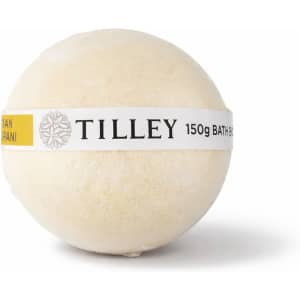 A bath bomb in a round shape, cream-coloured with a yellow label featuring branding.