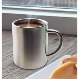 A stainless steel coffee mug with steam rising from the hot beverage inside, positioned near a plate of pancakes.